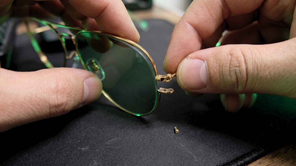 Hands sliding a teardrop replacement lens into the opened metal rim of an aviator frame