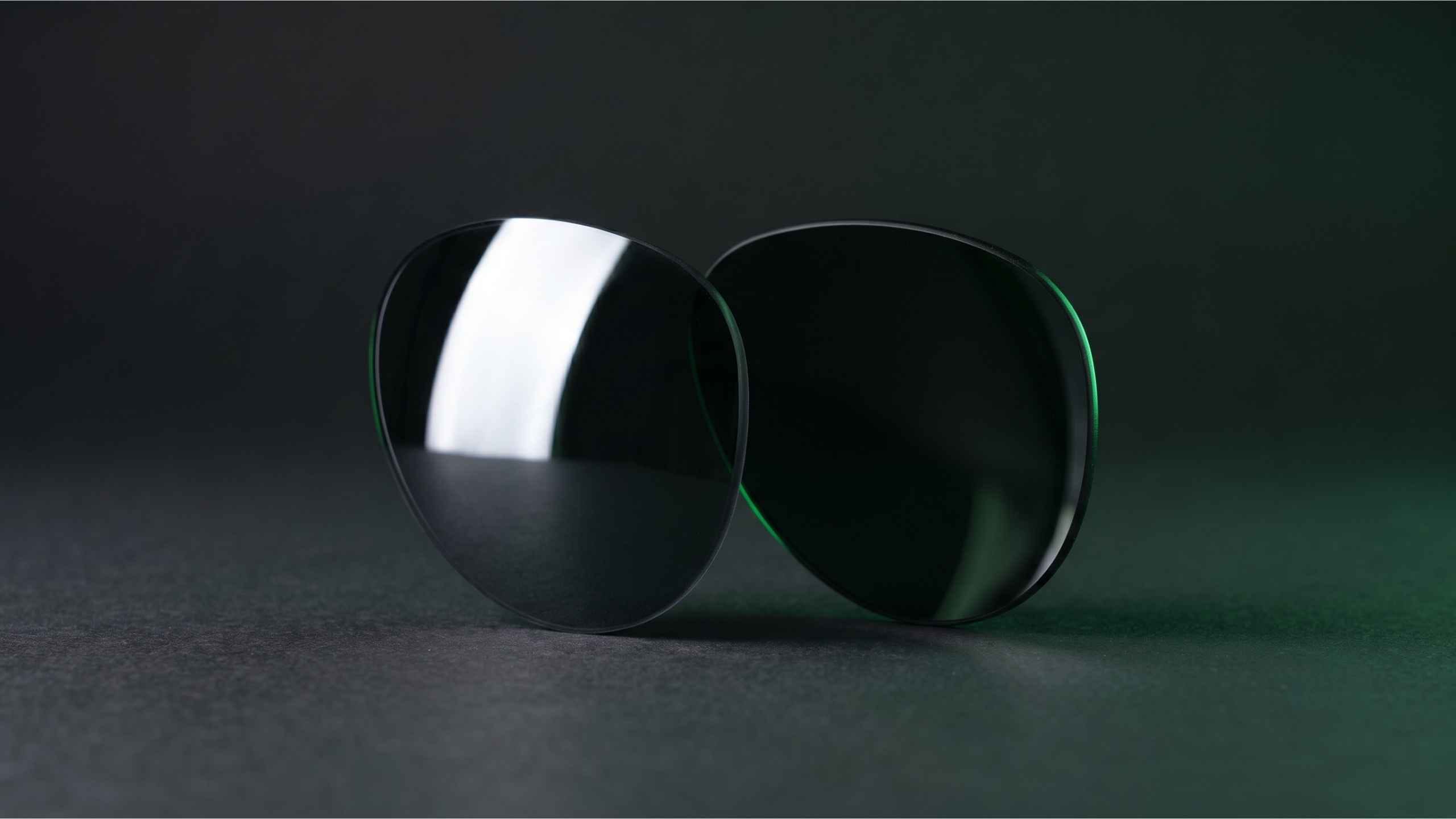 Two sunglass lenses side by side reflecting light differently on a dark surface
