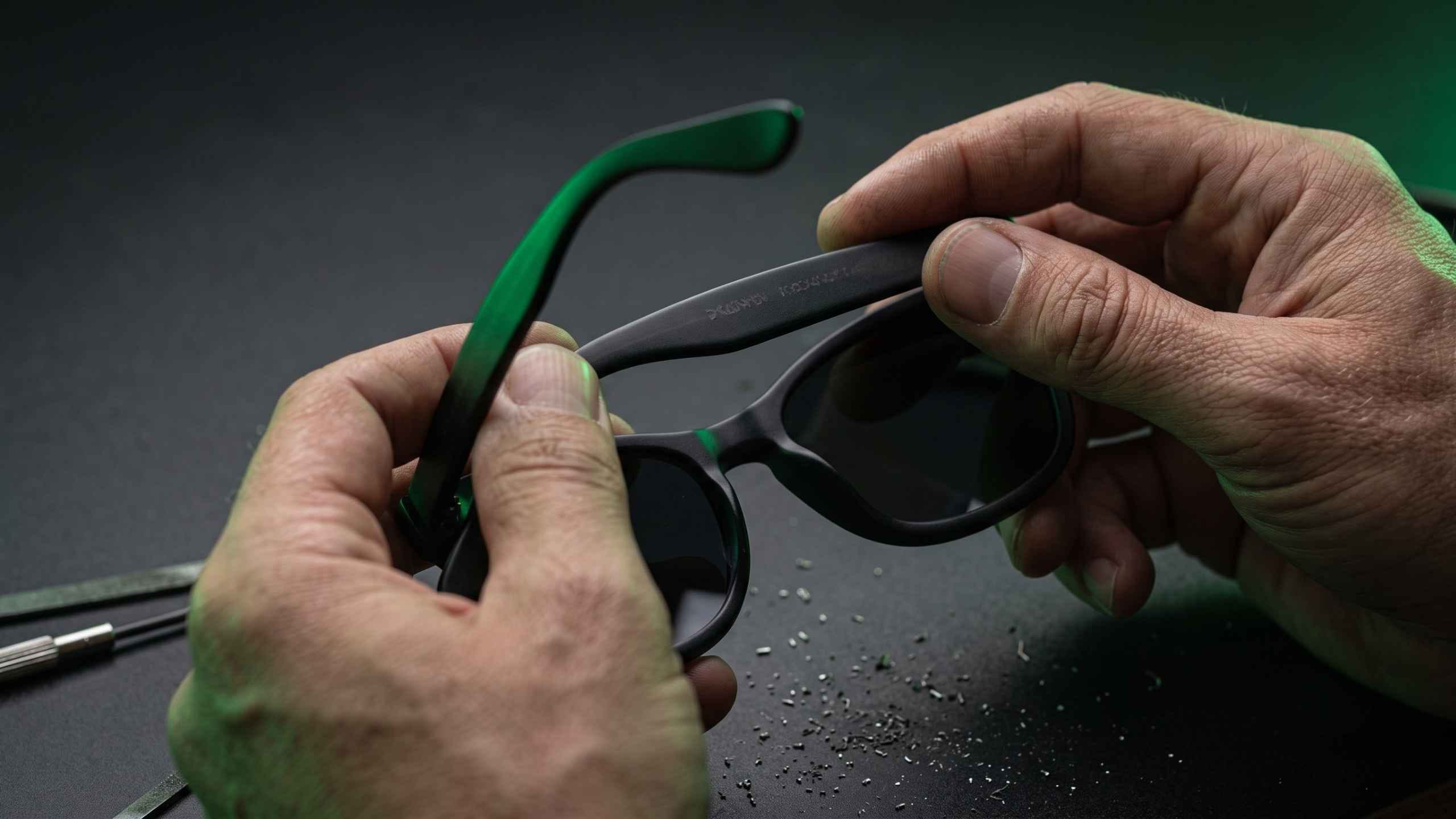 Hands holding an acetate sunglasses frame open to inspect the inside of the left temple arm