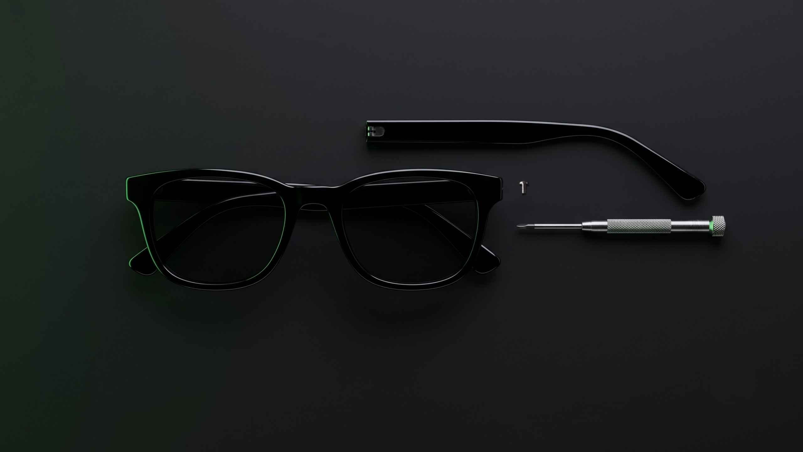 Detached temple arm beside a sunglasses frame and a precision screwdriver on a dark surface