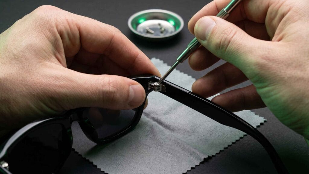 Hands fastening a hinge screw to attach a new temple arm to a sunglasses frame