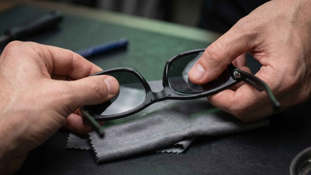 Hands separating a lens from a damp black acetate sunglasses frame over a microfiber cloth